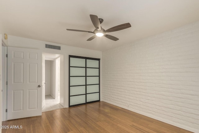 unfurnished bedroom with wood-type flooring, ceiling fan, and brick wall