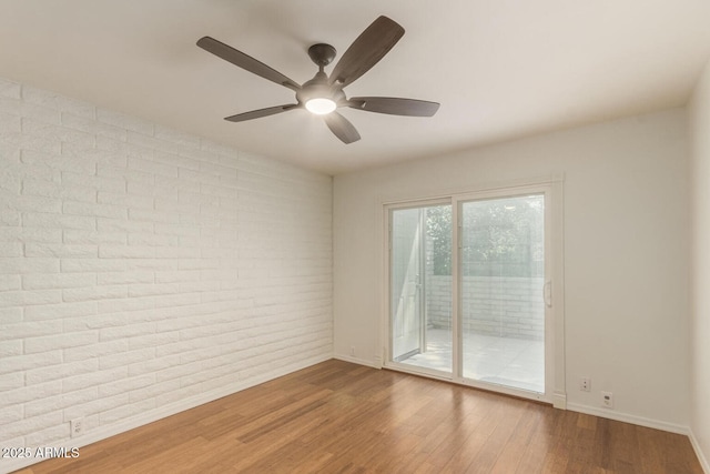 unfurnished room with ceiling fan, brick wall, and hardwood / wood-style floors