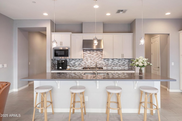 kitchen featuring built in microwave, white cabinetry, pendant lighting, and an island with sink