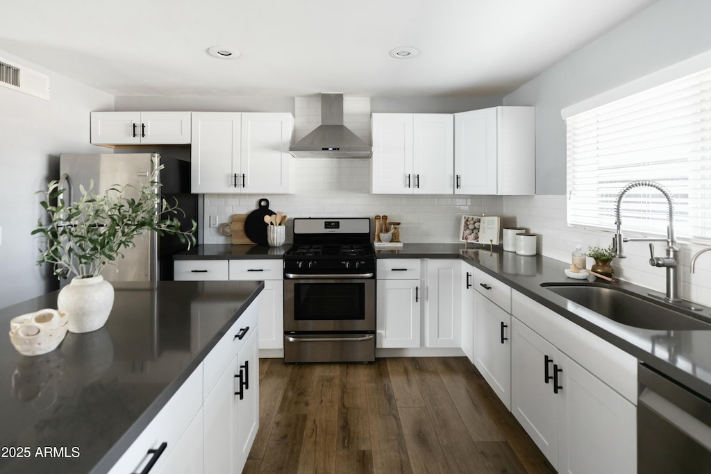 kitchen with white cabinetry, sink, wall chimney exhaust hood, dark hardwood / wood-style flooring, and appliances with stainless steel finishes