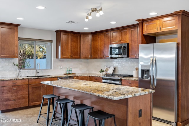 kitchen with sink, stainless steel appliances, a center island, light stone counters, and a kitchen bar