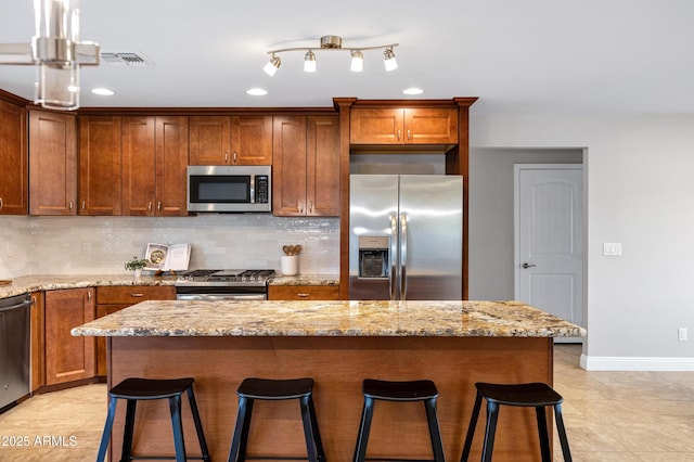 kitchen featuring appliances with stainless steel finishes, a center island, a breakfast bar area, and light stone counters