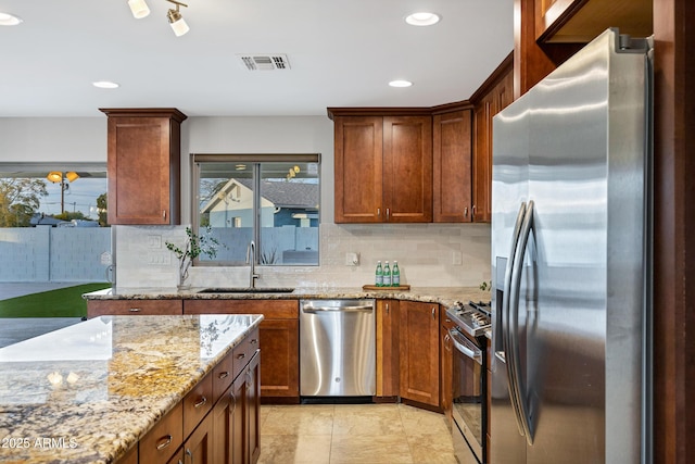 kitchen with sink, decorative backsplash, stainless steel appliances, and light stone countertops