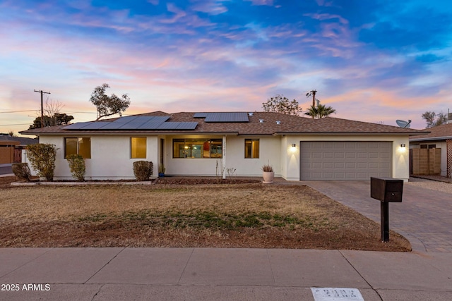 ranch-style home featuring a garage, a lawn, and solar panels