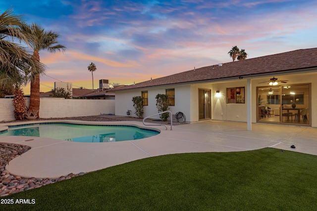 pool at dusk featuring a patio, ceiling fan, and a lawn