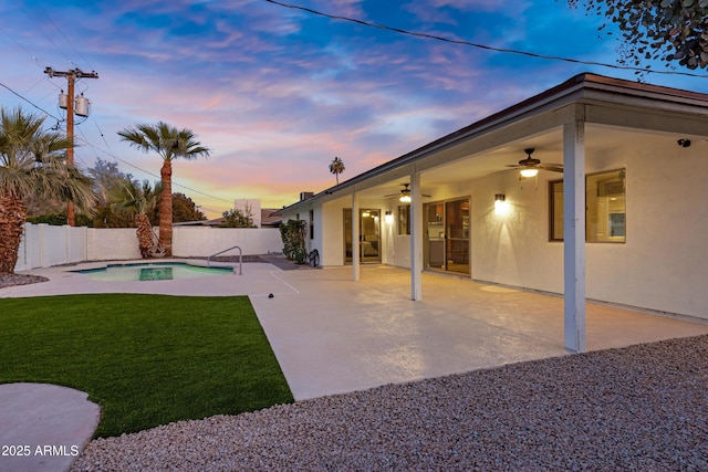 pool at dusk with a lawn, ceiling fan, and a patio area