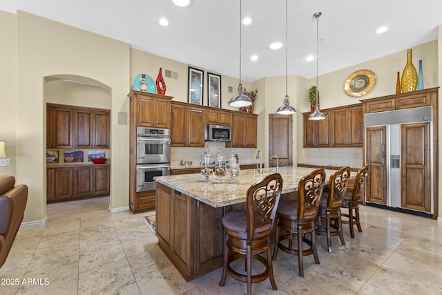 kitchen featuring appliances with stainless steel finishes, decorative backsplash, arched walkways, recessed lighting, and light stone counters