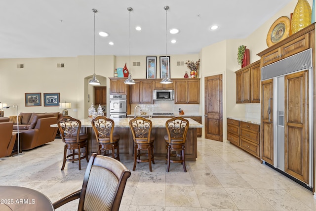 kitchen with stainless steel appliances, backsplash, light stone counters, a breakfast bar, and recessed lighting