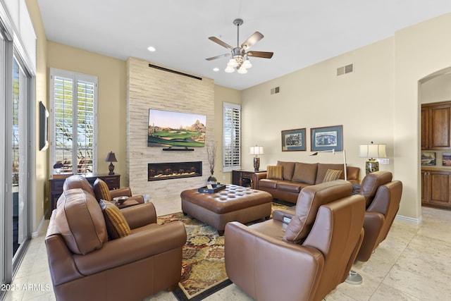 living area with a fireplace, ceiling fan, arched walkways, recessed lighting, and baseboards