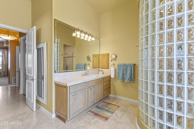 full bathroom with a tile shower, baseboards, vanity, a high ceiling, and tile patterned flooring