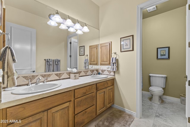 bathroom featuring toilet, double vanity, tasteful backsplash, and baseboards