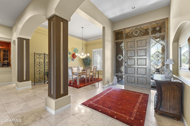 tiled entryway with decorative columns, arched walkways, baseboards, and a chandelier