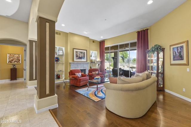 living room featuring arched walkways, recessed lighting, wood finished floors, baseboards, and a tiled fireplace
