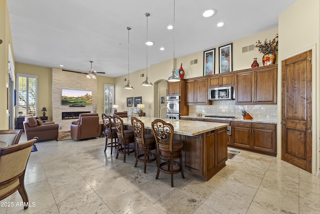 kitchen featuring appliances with stainless steel finishes, open floor plan, backsplash, a breakfast bar area, and light stone counters