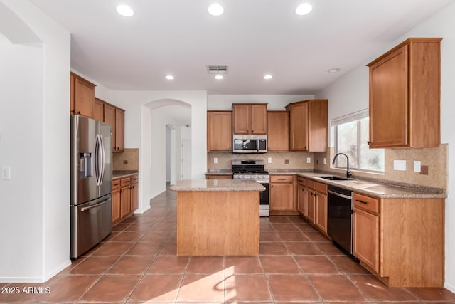 kitchen featuring sink, appliances with stainless steel finishes, a kitchen island, light stone countertops, and tile patterned flooring