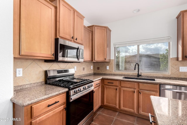 kitchen with sink, stainless steel appliances, light stone countertops, dark tile patterned flooring, and decorative backsplash