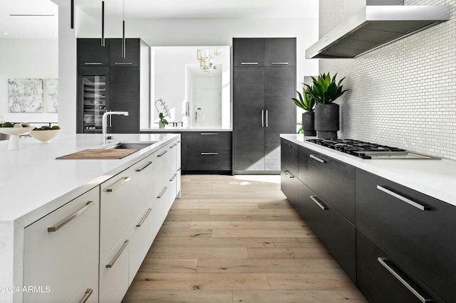 kitchen with gas cooktop, tasteful backsplash, wall chimney range hood, light hardwood / wood-style floors, and white cabinetry