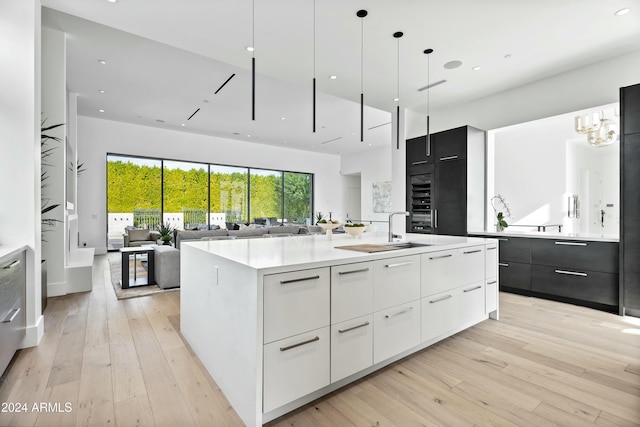 kitchen featuring white cabinets, a center island with sink, sink, decorative light fixtures, and light hardwood / wood-style floors