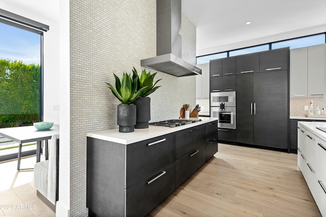 kitchen featuring backsplash, light hardwood / wood-style flooring, wall chimney exhaust hood, white cabinetry, and stainless steel appliances