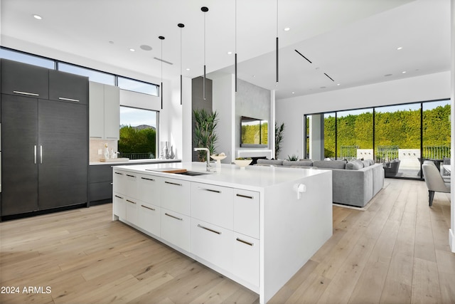 kitchen with pendant lighting, a kitchen island with sink, white cabinets, sink, and light hardwood / wood-style flooring