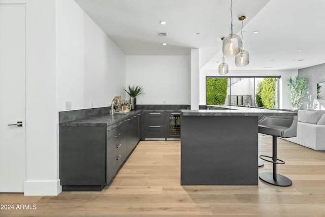 kitchen with beverage cooler, hanging light fixtures, kitchen peninsula, a kitchen bar, and light wood-type flooring