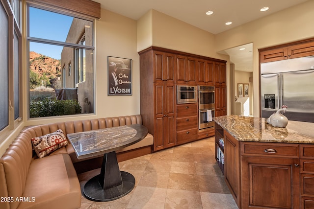 kitchen with appliances with stainless steel finishes, brown cabinetry, recessed lighting, and light stone countertops