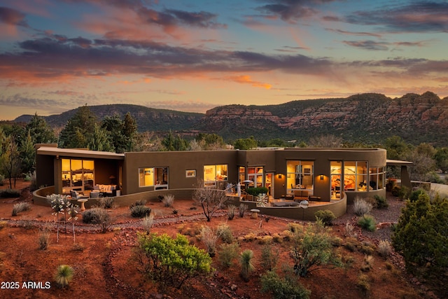 back of house at dusk featuring a patio area, a mountain view, and stucco siding