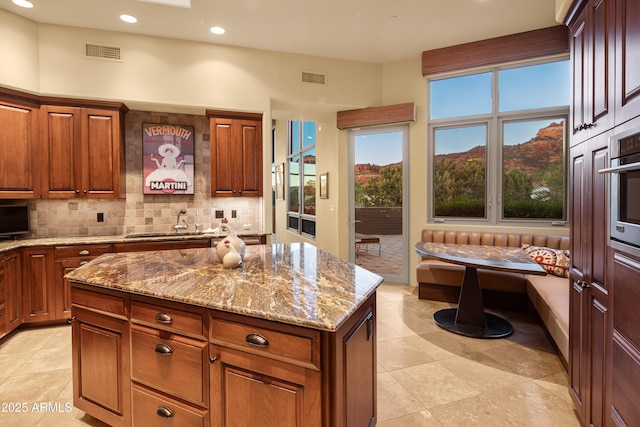 kitchen featuring visible vents, breakfast area, light stone counters, and backsplash