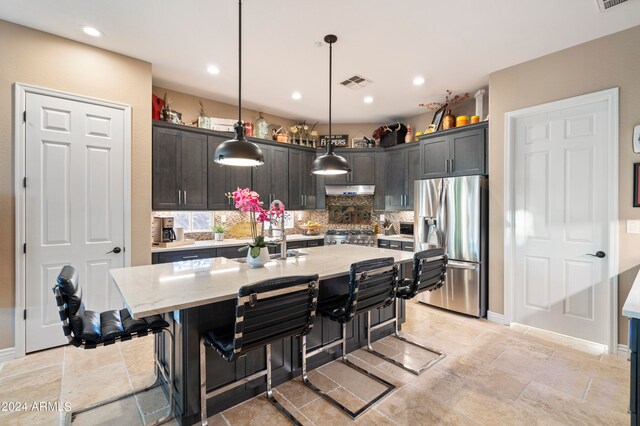 kitchen with stainless steel fridge, stove, a kitchen island with sink, pendant lighting, and a breakfast bar area