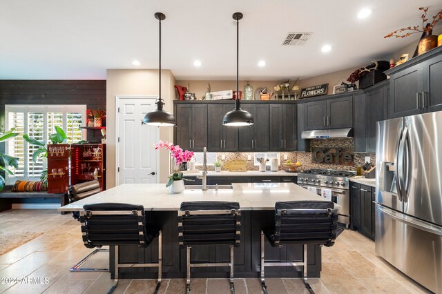 kitchen with a kitchen breakfast bar, backsplash, an island with sink, pendant lighting, and appliances with stainless steel finishes