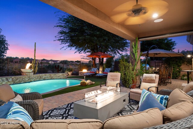 patio terrace at dusk with ceiling fan, a fenced in pool, and an outdoor living space with a fire pit