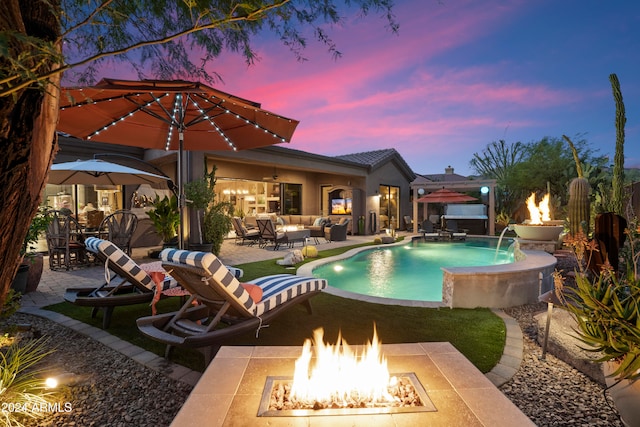 pool at dusk featuring pool water feature, a patio, and an outdoor living space with a fire pit