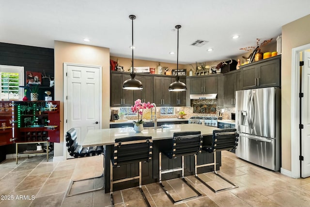 kitchen featuring decorative backsplash, dark brown cabinetry, decorative light fixtures, stainless steel fridge with ice dispenser, and an island with sink