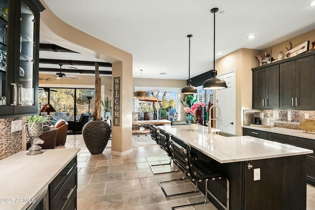 kitchen featuring tasteful backsplash, sink, beam ceiling, pendant lighting, and a center island with sink