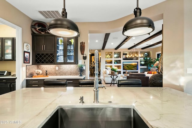 kitchen featuring pendant lighting, backsplash, light stone countertops, beamed ceiling, and dishwashing machine