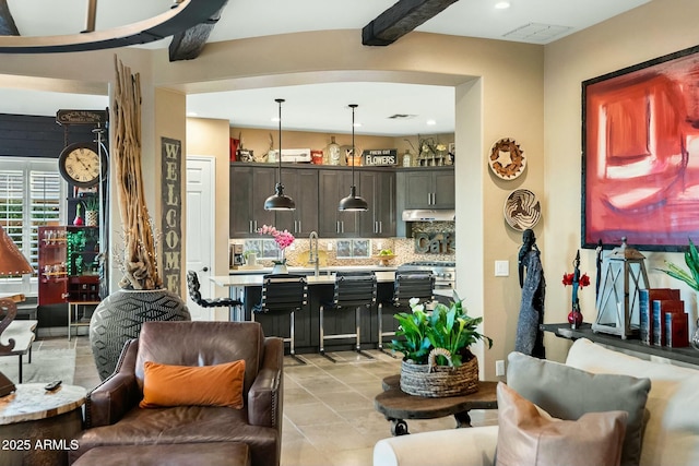 kitchen featuring decorative backsplash, a kitchen bar, dark brown cabinets, beamed ceiling, and hanging light fixtures