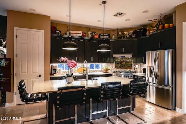 kitchen with stove, a center island with sink, a kitchen breakfast bar, hanging light fixtures, and stainless steel fridge with ice dispenser