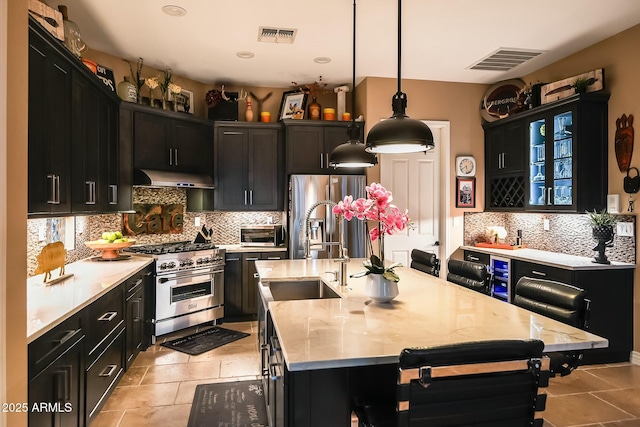 kitchen featuring decorative light fixtures, stainless steel appliances, a breakfast bar area, and an island with sink