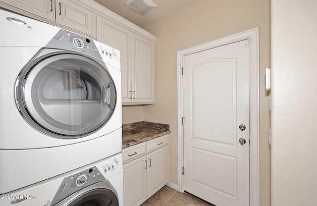 laundry area featuring stacked washer / drying machine, cabinets, and light tile patterned flooring