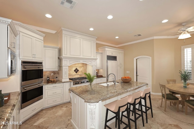 kitchen featuring sink, a center island with sink, light stone counters, and appliances with stainless steel finishes