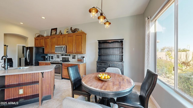 kitchen featuring appliances with stainless steel finishes, brown cabinetry, light countertops, and decorative light fixtures