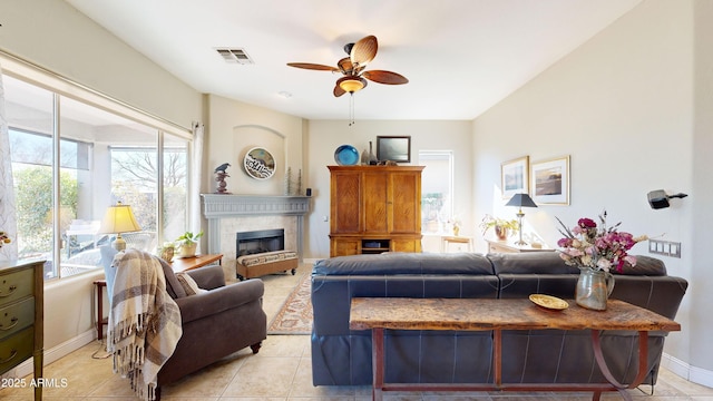 living room featuring ceiling fan, light tile patterned floors, visible vents, baseboards, and a glass covered fireplace