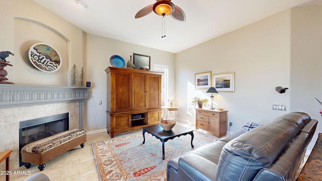 living area featuring light tile patterned floors, ceiling fan, baseboards, and a tile fireplace