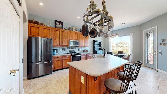 kitchen featuring stainless steel appliances, a sink, a kitchen island with sink, and brown cabinets