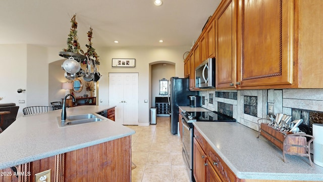 kitchen with arched walkways, stainless steel appliances, light countertops, a kitchen island with sink, and a sink