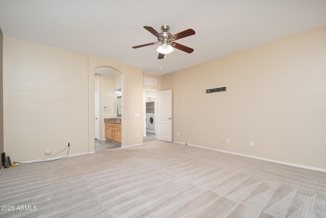 unfurnished bedroom featuring arched walkways, visible vents, light carpet, ensuite bath, and washer / dryer