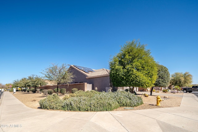 view of property exterior with a tile roof, roof mounted solar panels, fence, and stucco siding