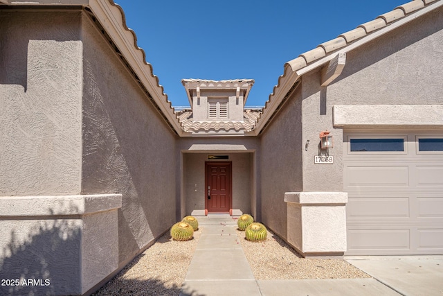 entrance to property featuring a garage, a tile roof, and stucco siding