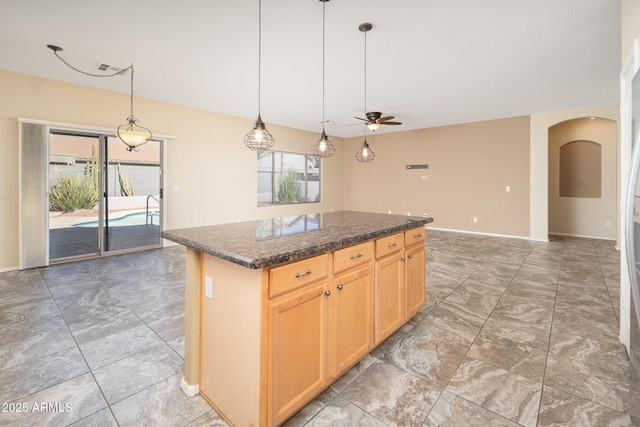 kitchen featuring arched walkways, pendant lighting, a center island, light brown cabinetry, and dark stone countertops