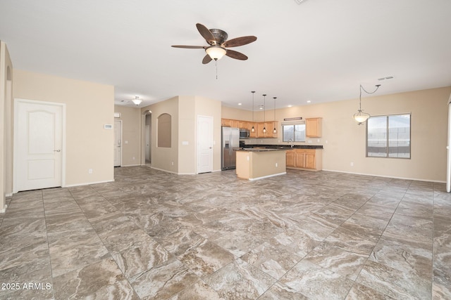 unfurnished living room with arched walkways, a sink, visible vents, a ceiling fan, and baseboards